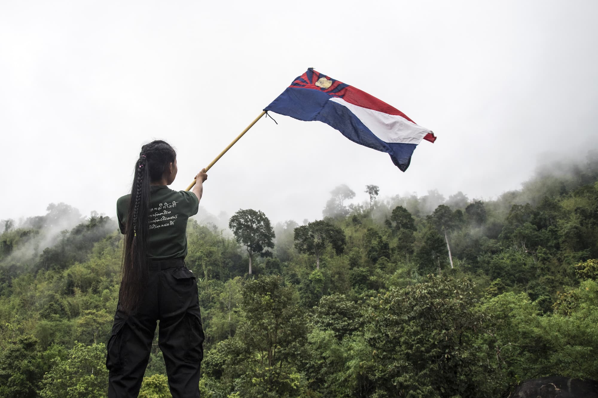 A young woman undergoing military training waves the flag of the Karen National Union (KNU) in Hpapun Township, Myanmar.
